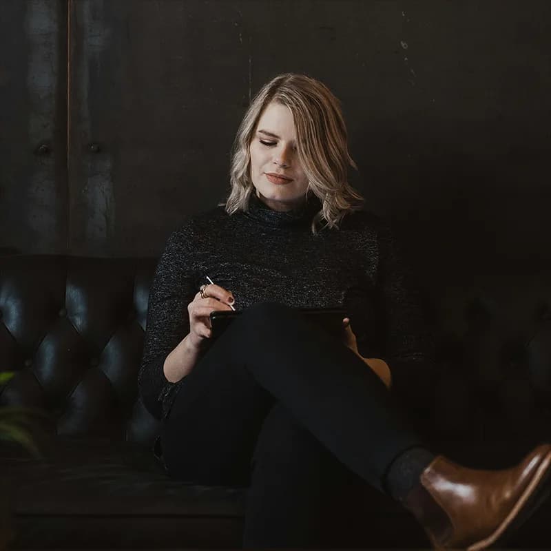 A focused woman sits on a leather sofa, using a stylus to write on a tablet.