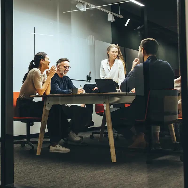 A professional team collaborating during a meeting in a modern conference room with glass walls.